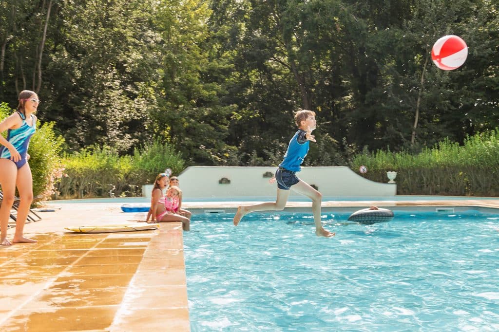 Camping Piscine Sarthe - Camping Château de Chanteloup : jeune garçon qui saute dans l'eau avec un ballon